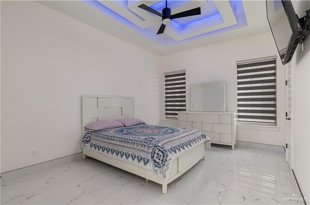 bedroom featuring marble finish floor, baseboards, a tray ceiling, and ceiling fan