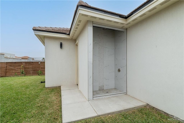 view of exterior entry with a patio area, fence, a lawn, and stucco siding