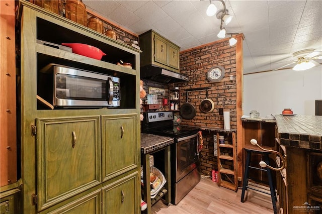 kitchen featuring green cabinets, light wood-type flooring, tile counters, stainless steel appliances, and brick wall