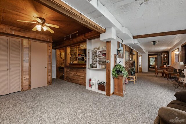 carpeted living room with wooden walls, beamed ceiling, and ceiling fan