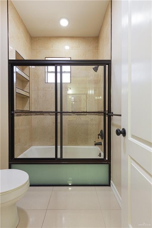 bathroom featuring tile patterned flooring, toilet, and combined bath / shower with glass door