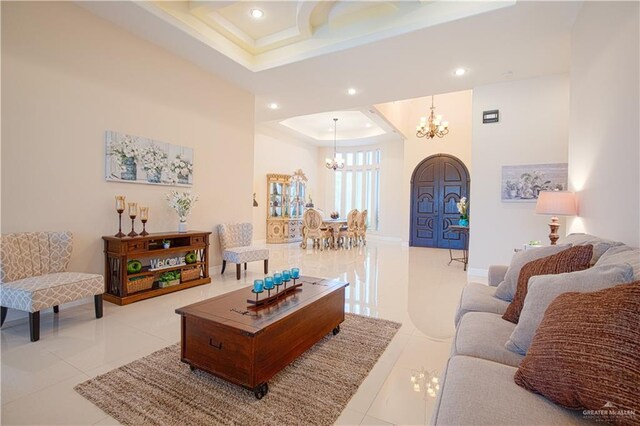 tiled living room featuring a tray ceiling, a high ceiling, and a notable chandelier