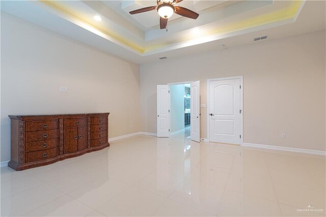 empty room featuring ceiling fan, a raised ceiling, and light tile patterned floors