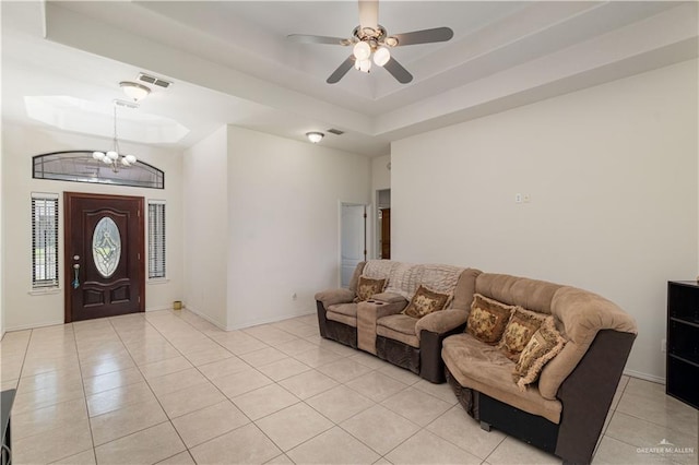 living room featuring ceiling fan with notable chandelier, light tile patterned floors, and a tray ceiling