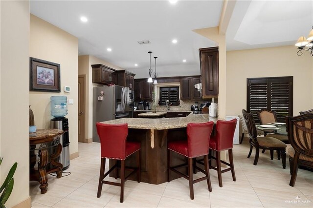 kitchen featuring decorative backsplash, a kitchen bar, kitchen peninsula, light stone countertops, and decorative light fixtures