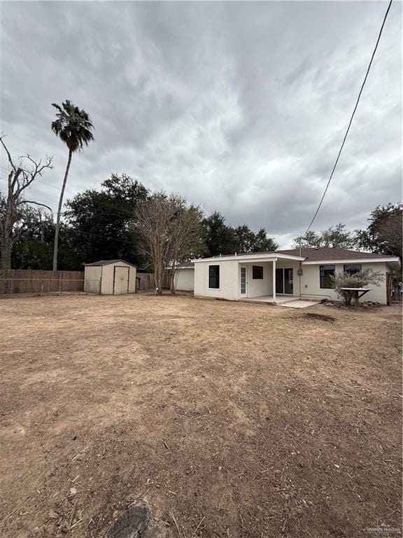 rear view of property with a storage shed, a patio area, fence, and an outdoor structure