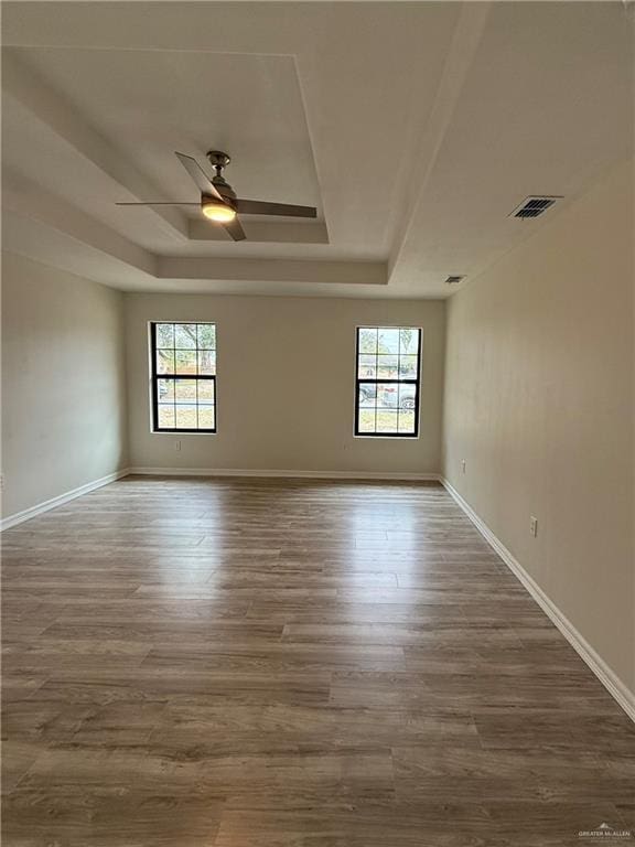 spare room featuring baseboards, a raised ceiling, and wood finished floors