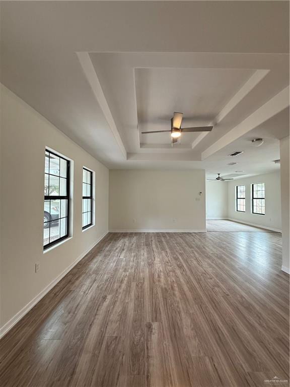 unfurnished living room with a tray ceiling, baseboards, and wood finished floors