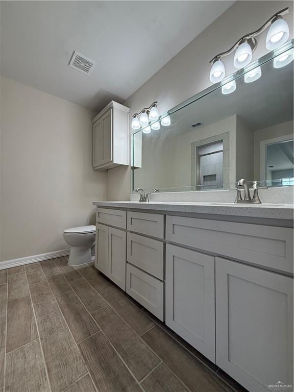 bathroom with wood finish floors, double vanity, visible vents, toilet, and a sink