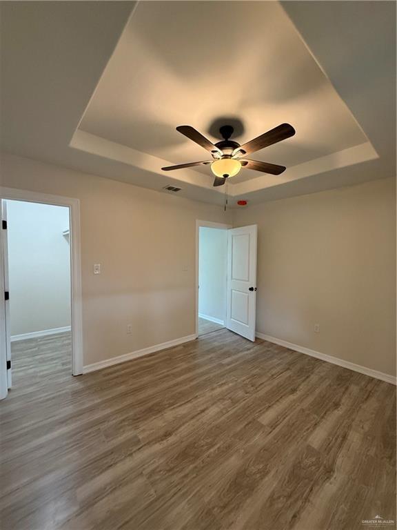 empty room with a tray ceiling, visible vents, baseboards, and wood finished floors