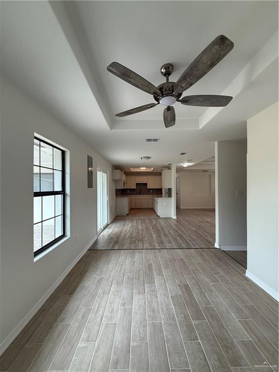 unfurnished living room with light wood-style flooring, visible vents, a tray ceiling, and baseboards