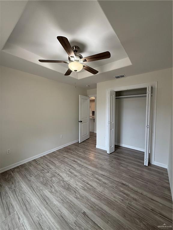 unfurnished bedroom featuring a tray ceiling, visible vents, baseboards, and wood finished floors