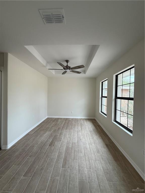 empty room featuring a raised ceiling, visible vents, a ceiling fan, wood finished floors, and baseboards