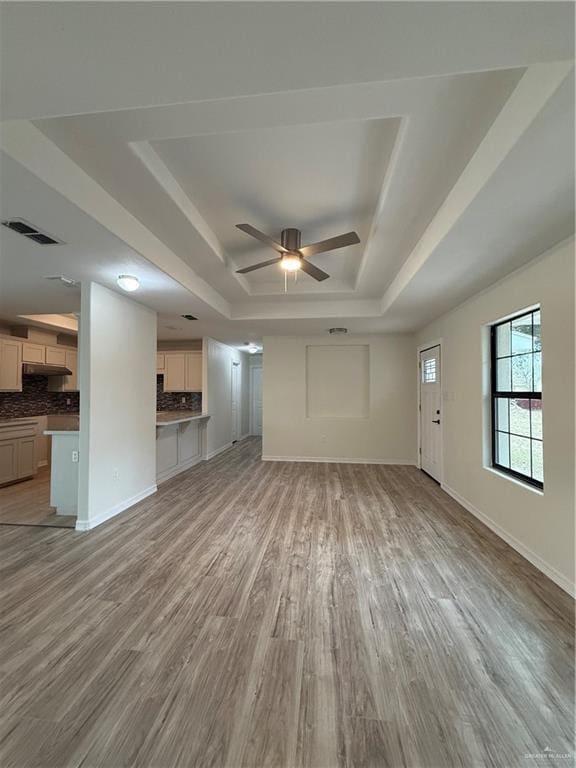 unfurnished living room featuring a tray ceiling, baseboards, visible vents, and light wood finished floors