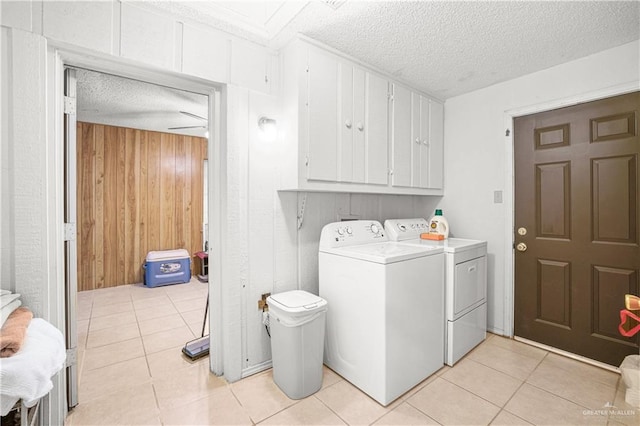 clothes washing area featuring cabinets, separate washer and dryer, a textured ceiling, wooden walls, and light tile patterned flooring