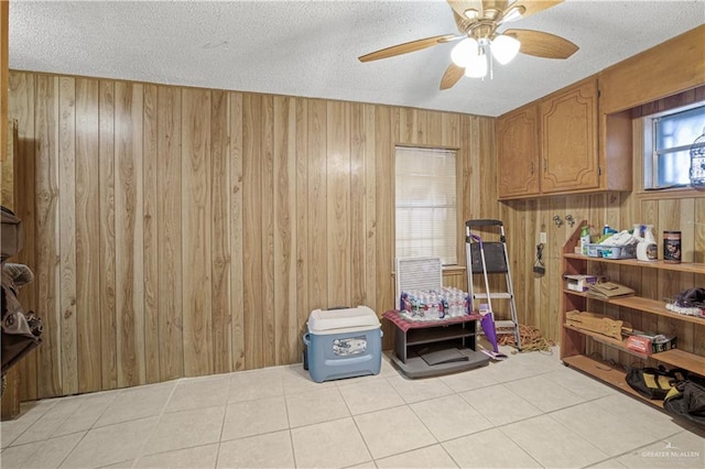 misc room featuring ceiling fan, light tile patterned floors, a textured ceiling, and wooden walls