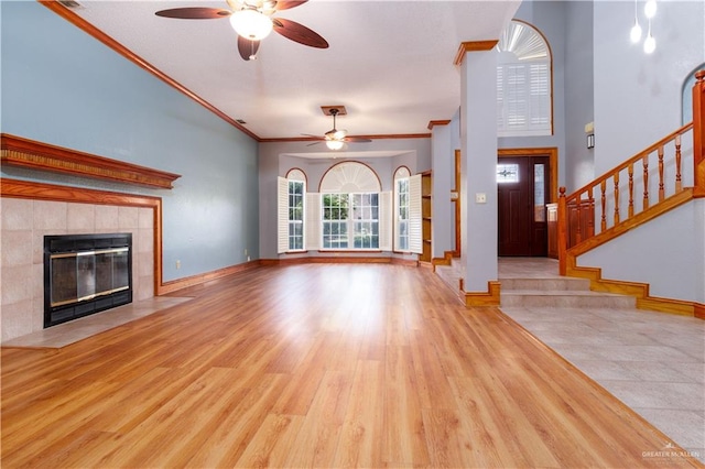 unfurnished living room featuring a tile fireplace, crown molding, ceiling fan, and light hardwood / wood-style floors