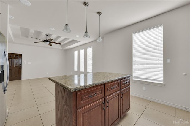 kitchen featuring a kitchen island, stone countertops, hanging light fixtures, light tile patterned floors, and a raised ceiling