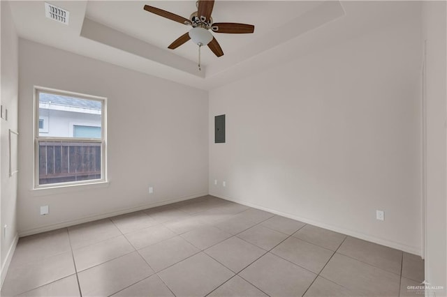 tiled empty room featuring ceiling fan, a tray ceiling, and electric panel