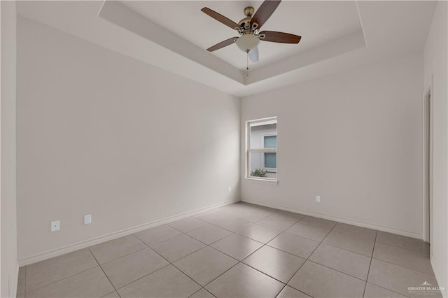 spare room with a raised ceiling, light tile patterned floors, and ceiling fan