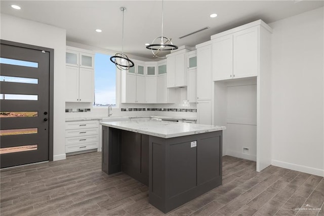 kitchen with a center island, white cabinetry, hanging light fixtures, light stone countertops, and a chandelier