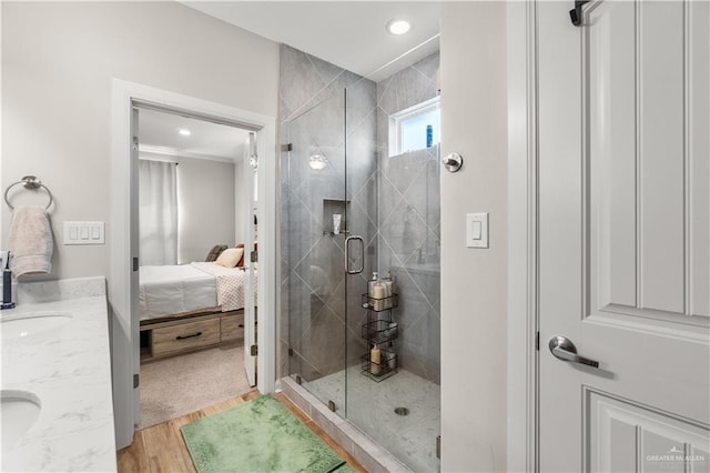 ensuite bathroom featuring a shower stall, wood finished floors, a sink, double vanity, and ensuite bath