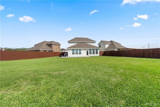 rear view of house featuring a fenced backyard, roof with shingles, and a yard
