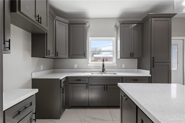 kitchen featuring a sink, gray cabinets, light stone counters, and marble finish floor