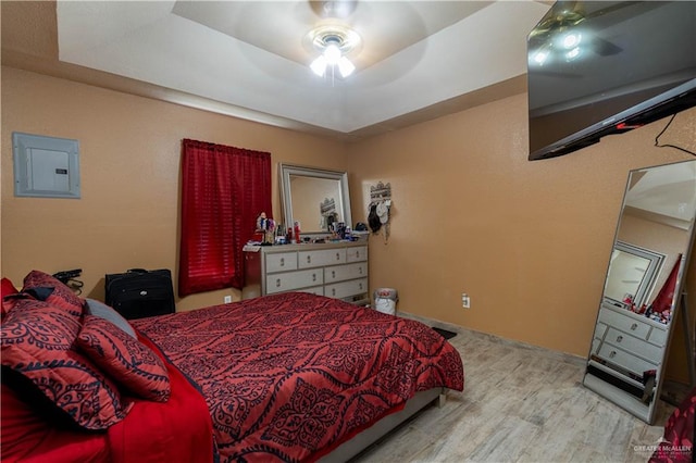 bedroom with ceiling fan, light wood-type flooring, electric panel, and a tray ceiling