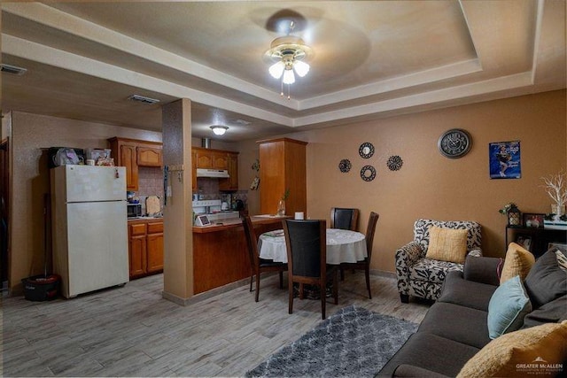 living room featuring ceiling fan, a raised ceiling, and light hardwood / wood-style flooring