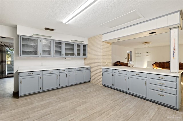 kitchen featuring gray cabinets, light hardwood / wood-style floors, a textured ceiling, and brick wall