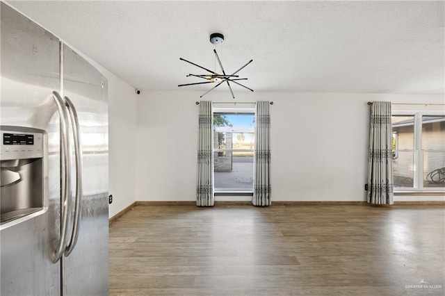 interior space with a textured ceiling, hardwood / wood-style floors, stainless steel refrigerator with ice dispenser, and a notable chandelier