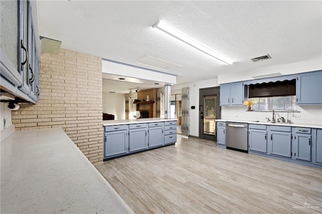 kitchen with sink, stainless steel dishwasher, brick wall, a textured ceiling, and light wood-type flooring