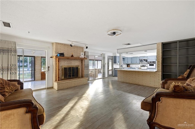 living room with a brick fireplace, track lighting, and hardwood / wood-style flooring