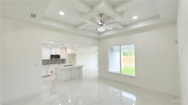 kitchen with white cabinetry, coffered ceiling, tasteful backsplash, beamed ceiling, and a center island with sink