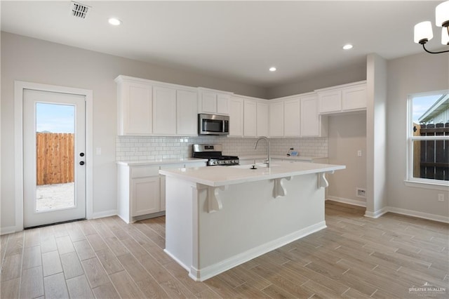 kitchen with stainless steel appliances, a center island with sink, and white cabinets