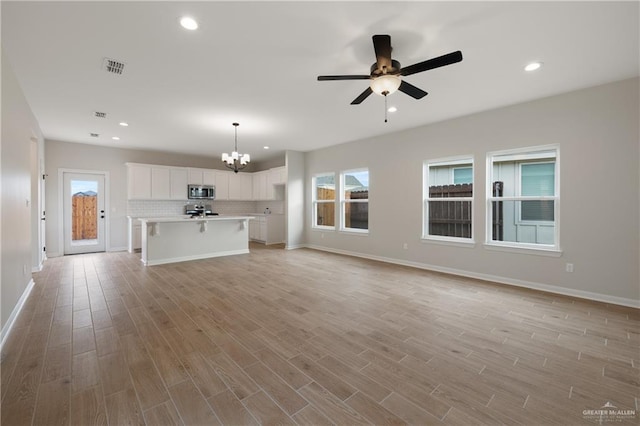 unfurnished living room with ceiling fan with notable chandelier and light wood-type flooring