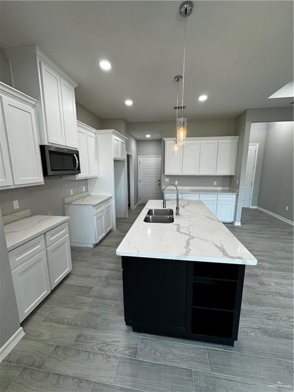 kitchen with white cabinetry, light stone countertops, sink, decorative light fixtures, and a center island with sink