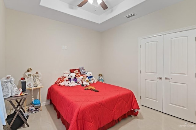 bedroom with ceiling fan, light tile patterned floors, a tray ceiling, and a closet