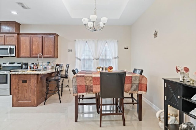 dining area featuring a raised ceiling, sink, and a chandelier