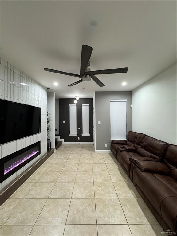 living room featuring light tile patterned floors, a large fireplace, and ceiling fan