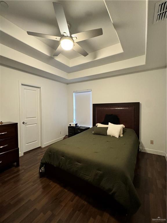 bedroom featuring dark wood-type flooring, ceiling fan, and a tray ceiling