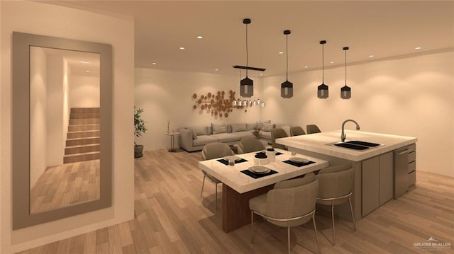 kitchen with a kitchen island with sink, a sink, light wood-style floors, and hanging light fixtures