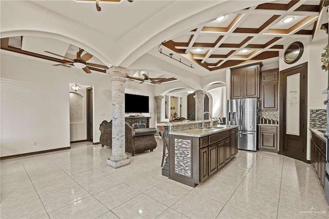 kitchen with a center island with sink, dark brown cabinets, stainless steel fridge with ice dispenser, and decorative columns