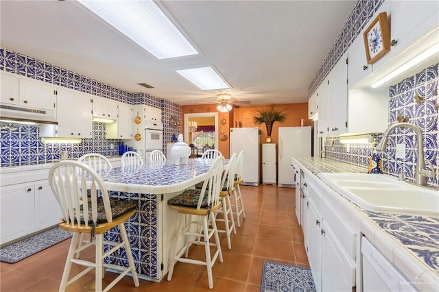 kitchen with sink, tile counters, a kitchen breakfast bar, white appliances, and white cabinets