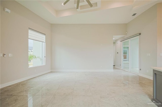 spare room with marble finish floor, a raised ceiling, visible vents, and baseboards