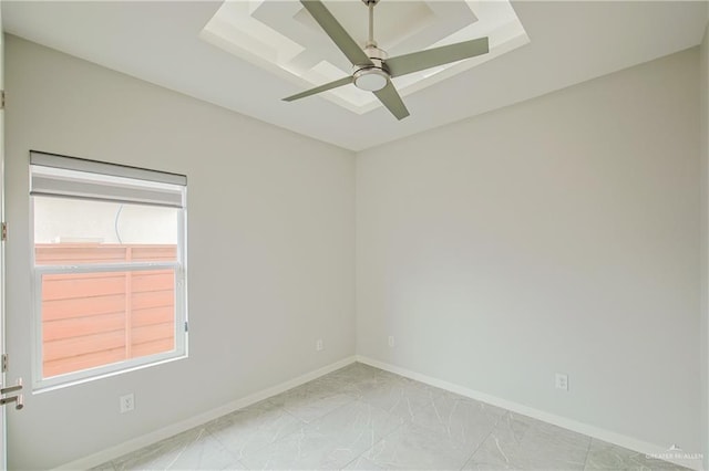 empty room with a ceiling fan, a tray ceiling, marble finish floor, and baseboards