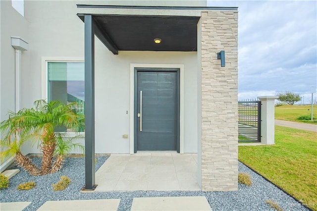 view of exterior entry featuring a lawn and stucco siding