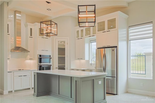 kitchen with stainless steel appliances, light countertops, wall chimney range hood, white cabinetry, and a sink