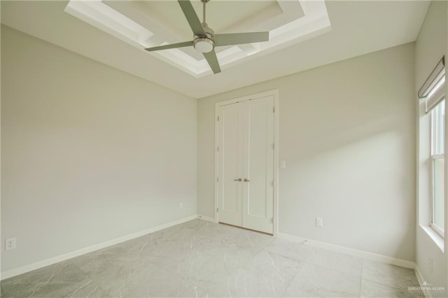 spare room with ceiling fan, a raised ceiling, and baseboards